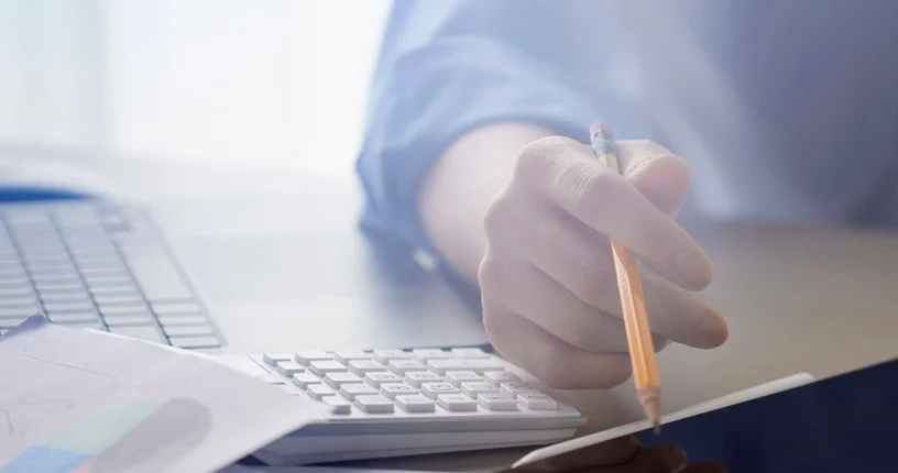 책상 위에 노트북, 계산기, 태블릿이 놓여있고 사람 손에 연필이 들려있는 모습
