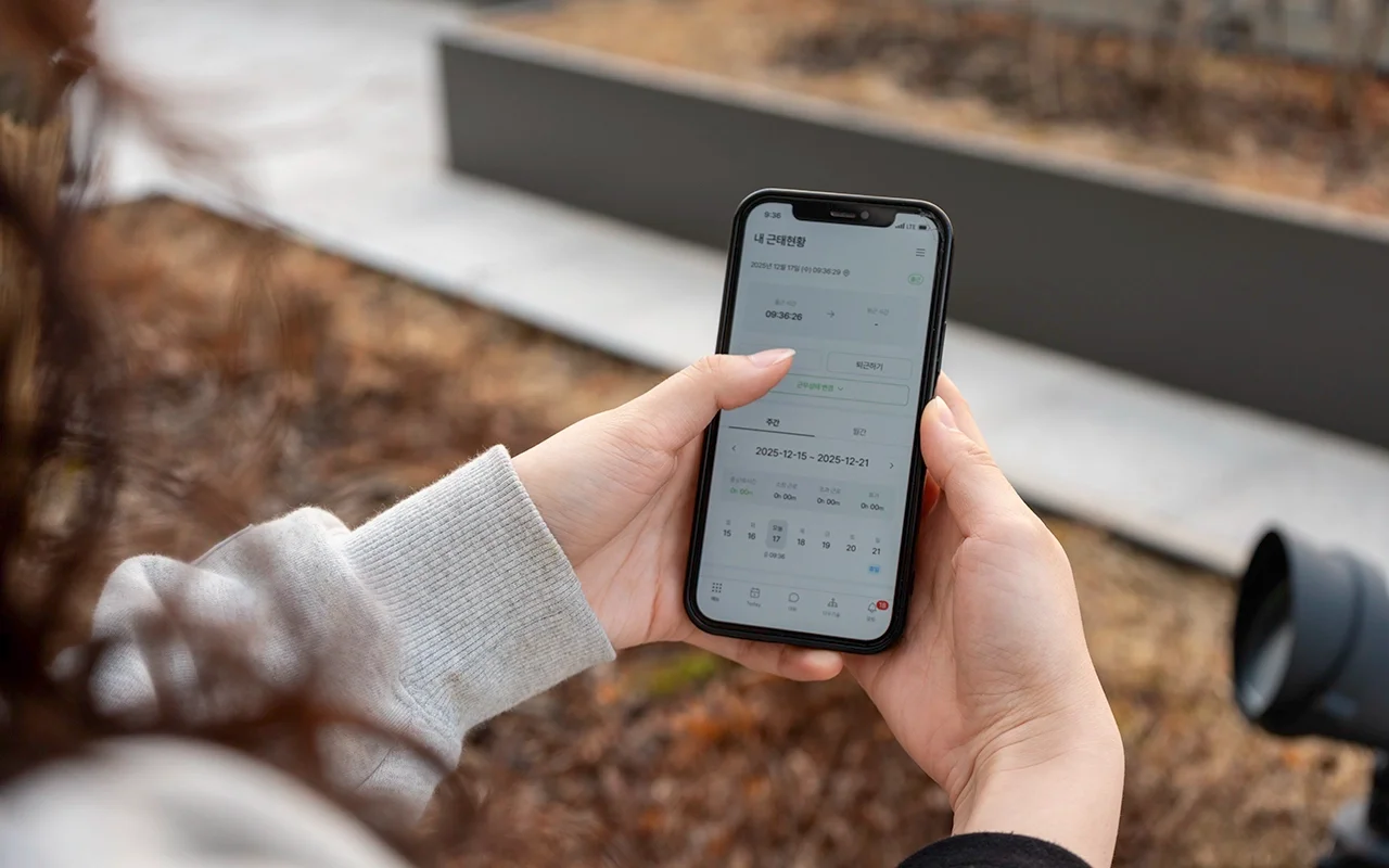 야외에서 모바일 앱으로 '출근하기' 버튼을 누르는 손 클로즈업 사진