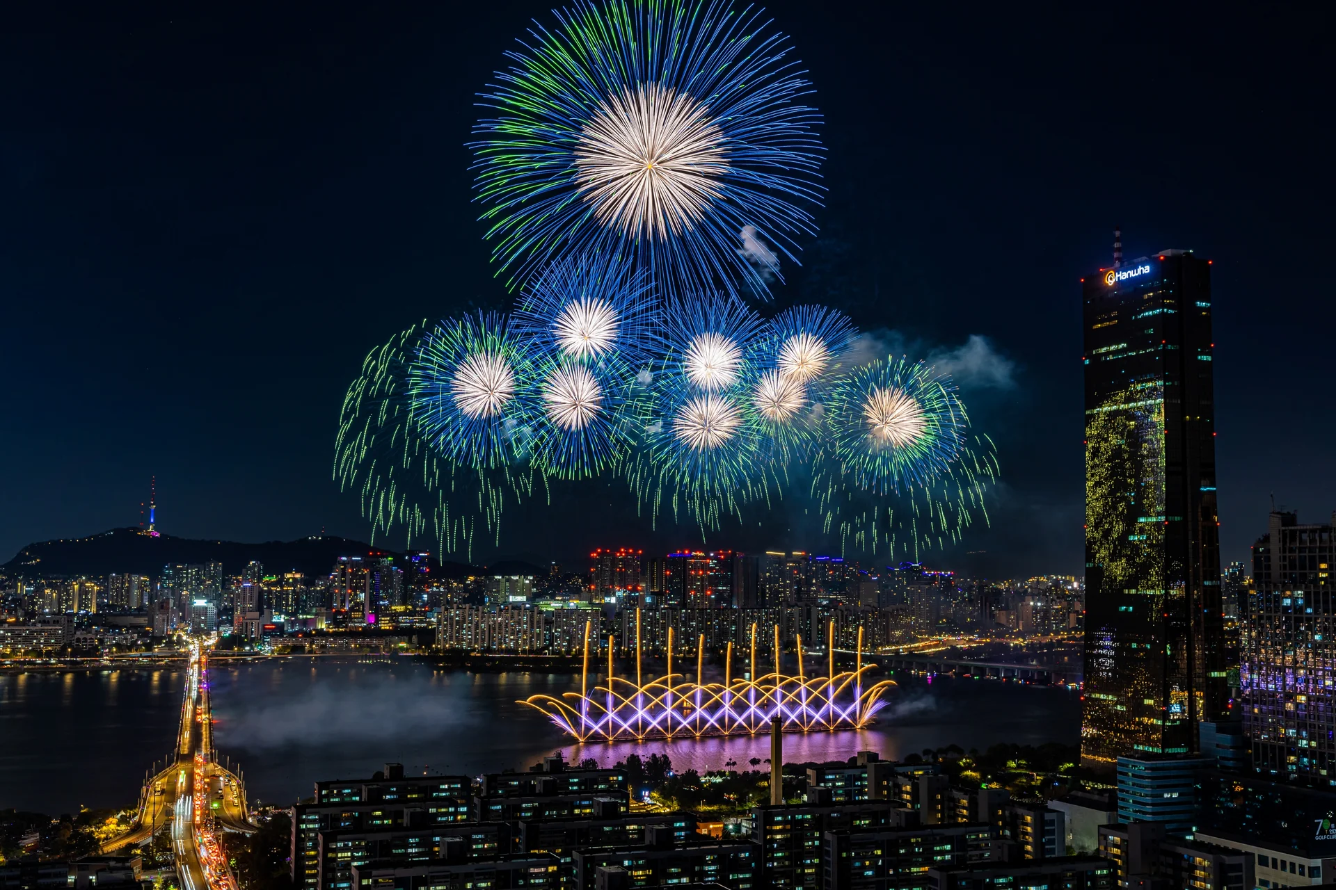 Night view of the Seoul International Fireworks Festival over the Han River, with vibrant fireworks lighting up the sky above Yeouido and the city skyline, including the iconic 63 Building.