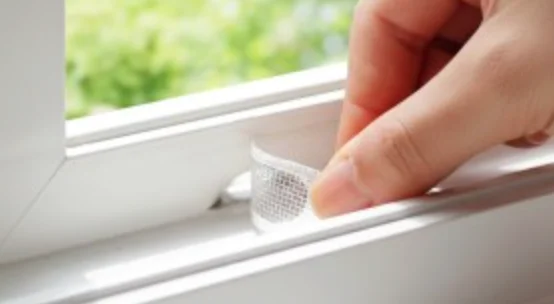 Hand placing a mesh sticker on a window track.