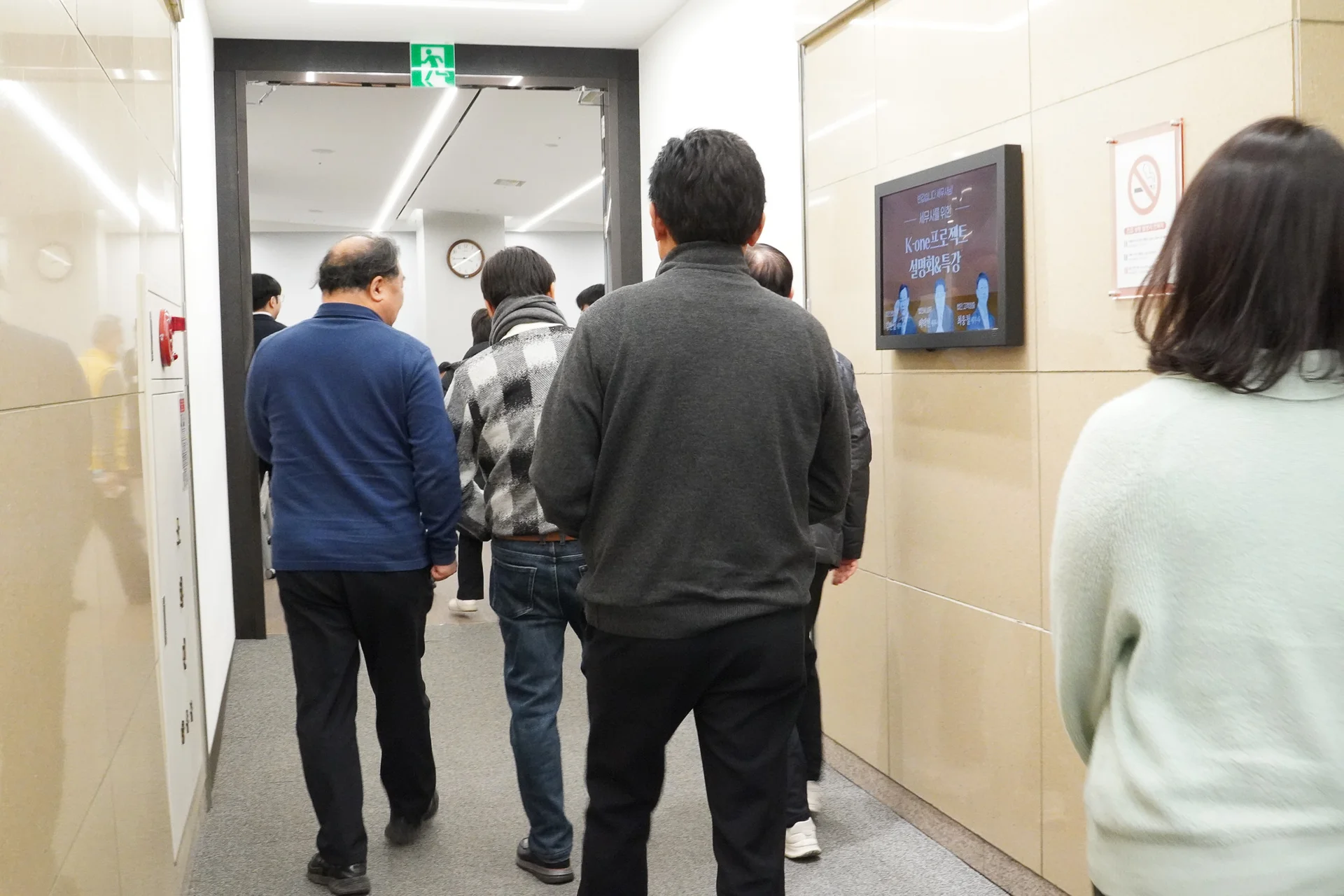 아이보리색 대리석 벽면과 회색 카펫이 깔린 복도, 그곳에서 설명회 참석을 위해 입장하고 있는 세무사들을 뒤편에서 촬영한 사진