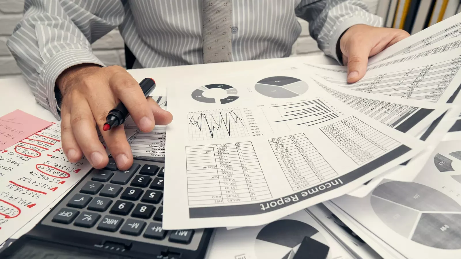 회계 문서와 계산기 앞에서 펜을 든 손, 재무 관련 자료를 검토하는 장면