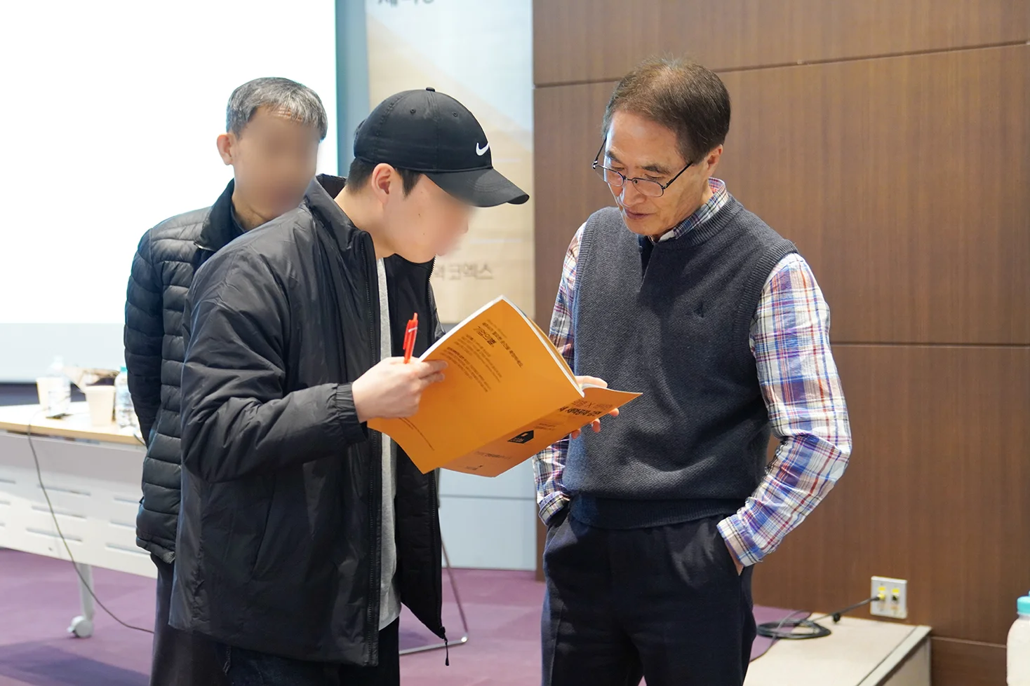 캡모자를 쓴 젊은 남성 세무사가 교재를 들고 배택현 세무사에게 질문하는 사진