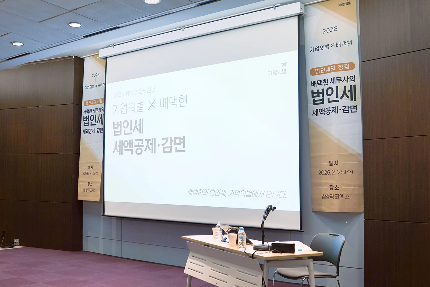 법인세 세액공제 감면 특강 대기화면의 띄워져있는 스크린이 중앙, 법인세 특강 현수막이 양옆에 있고 우측에 강사 책상이 세팅되어 있는 사진