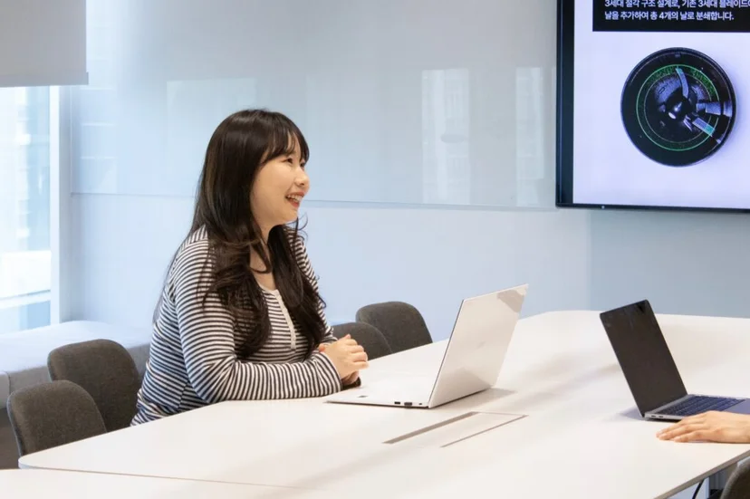 앳홈 팀원이 블레이드 도면 화면 배경으로 회의실에서 웃으며 인터뷰하는 모습