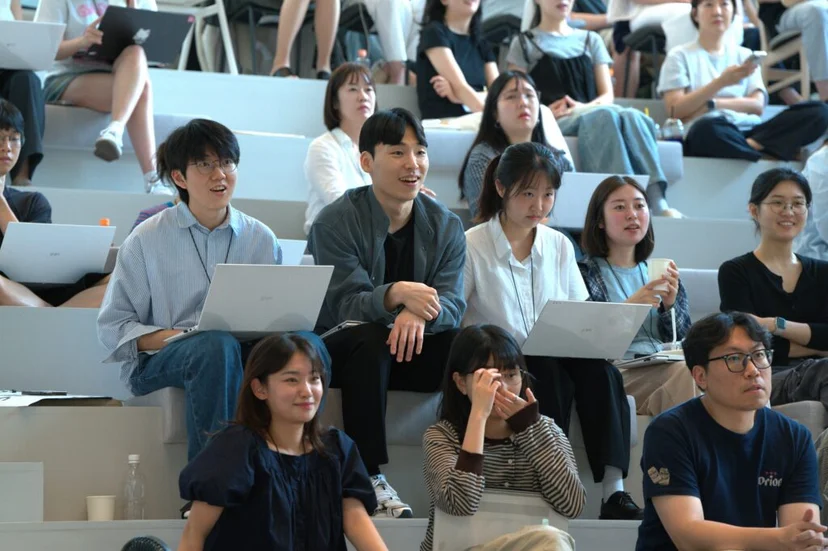 얼라이먼트 데이 계단식 좌석에서 앳홈 직원들이 웃으며 발표를 듣는 모습