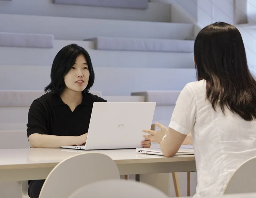 앳홈 팀원이 오피스 계단식 공용 공간에서 동료와 노트북을 앞에 두고 대화하는 모습