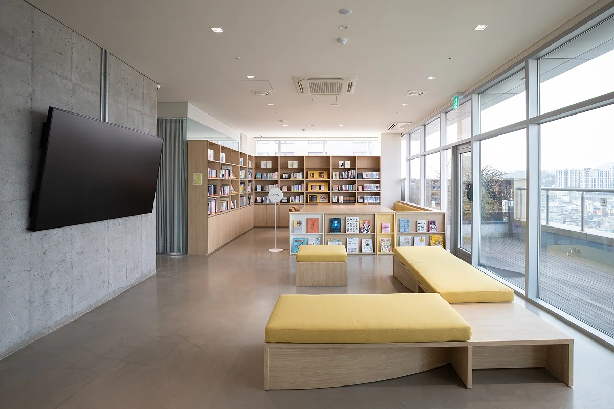 Mangrove residents' library lounge — floor-to-ceiling bookshelves, large screen, day beds, and panoramic city-view windows. Available 24/7 for studying, reading, or unwinding without leaving the building.