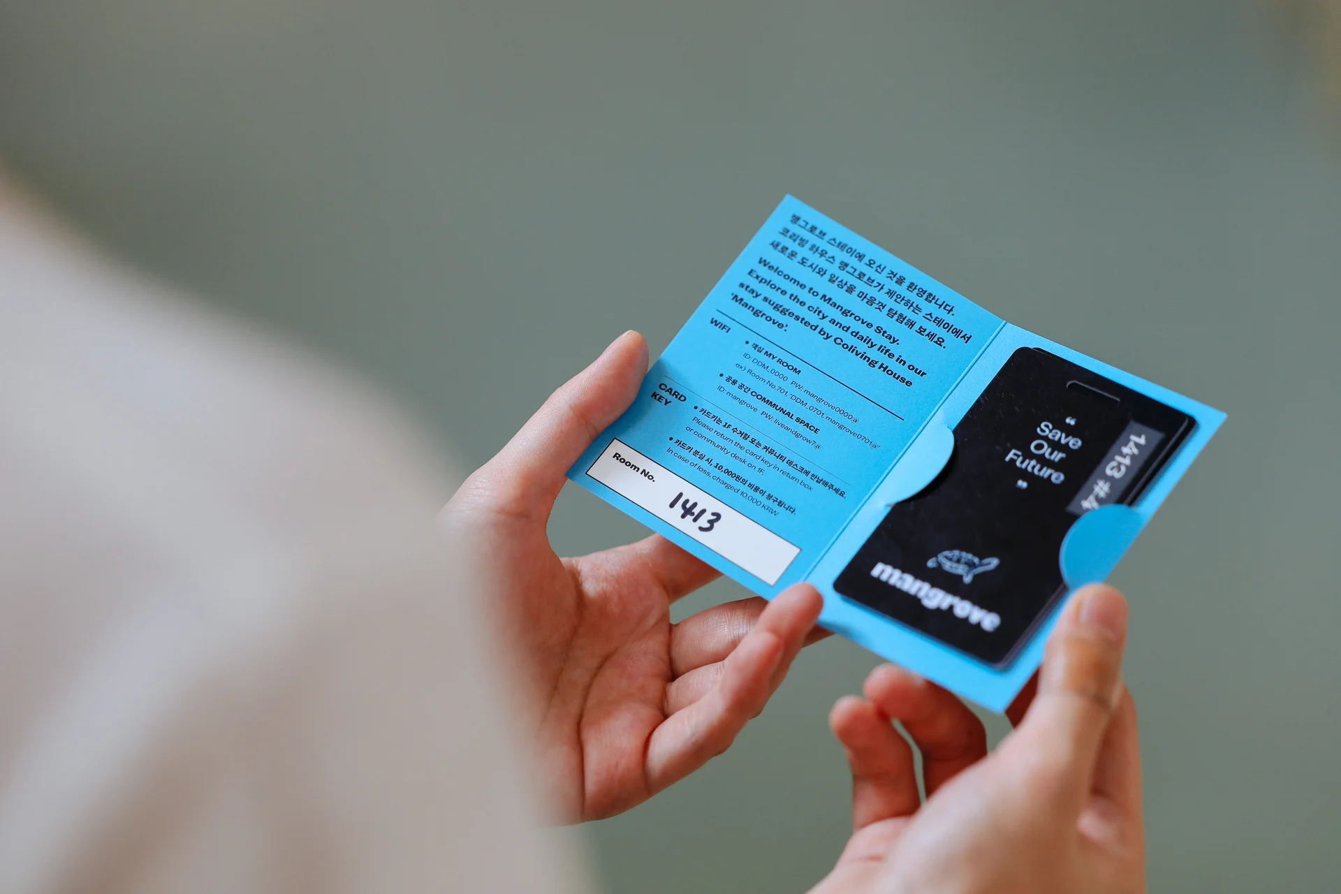 A resident holding a Mangrove branded key card packet — blue welcome booklet with room number and access card included, provided at move-in.