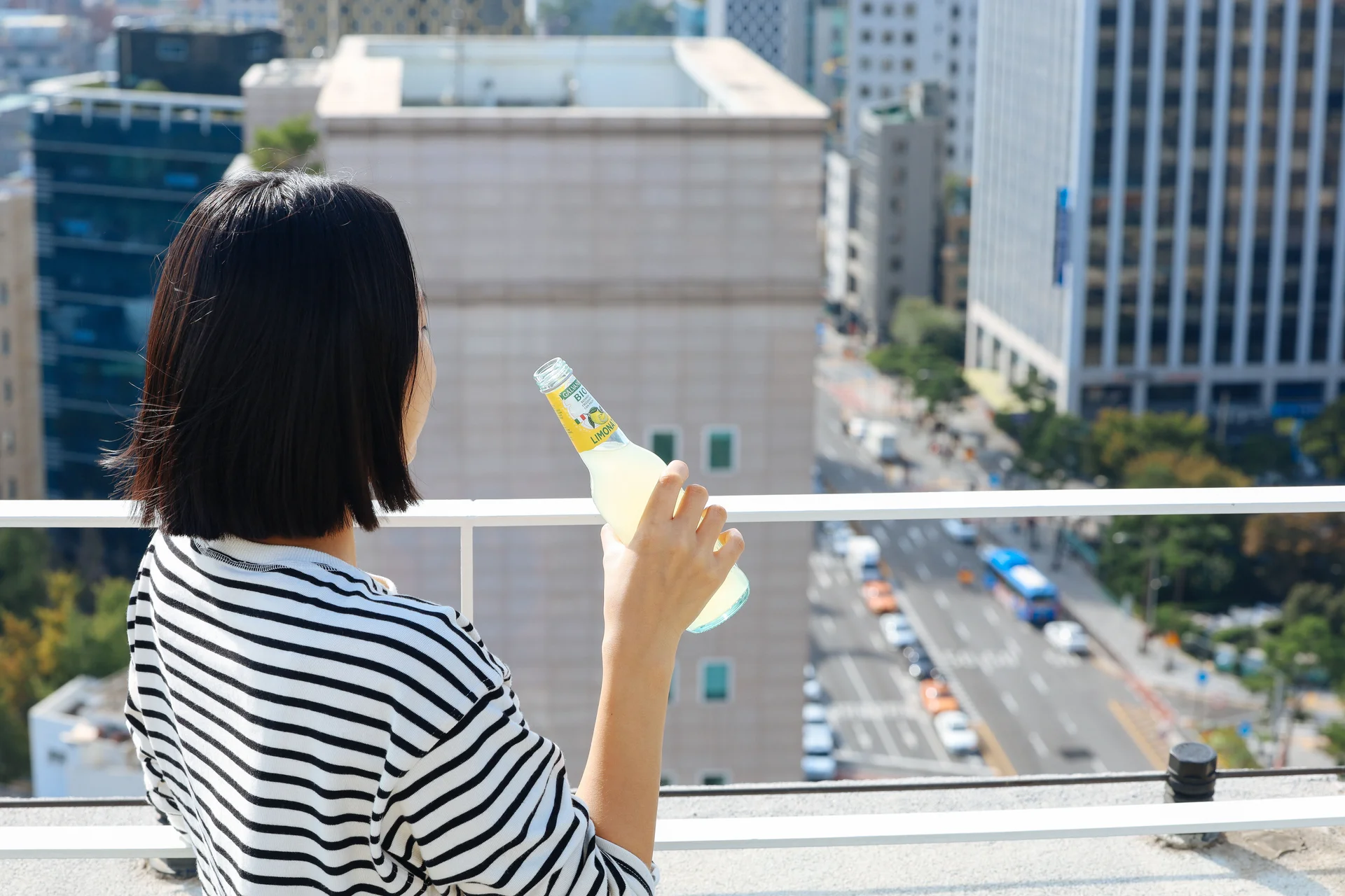 A Mangrove Dongdaemun resident enjoying a drink on the rooftop terrace, overlooking the Seoul city skyline and busy streets below on a clear autumn day.