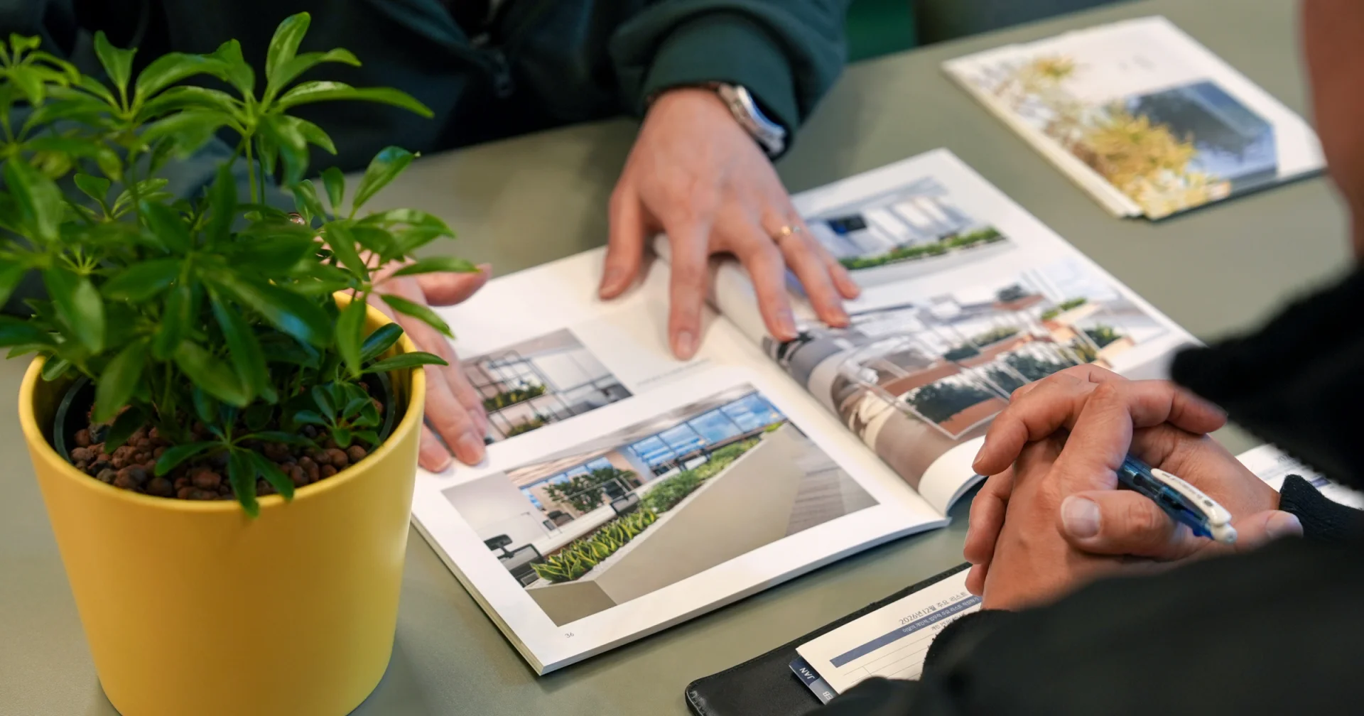 화분을 놓은 테이블 위에서 팸플렛을 보며 이야기중인 두 사람. 플랜테리어 컨설팅 중인 에코피플과 고객.