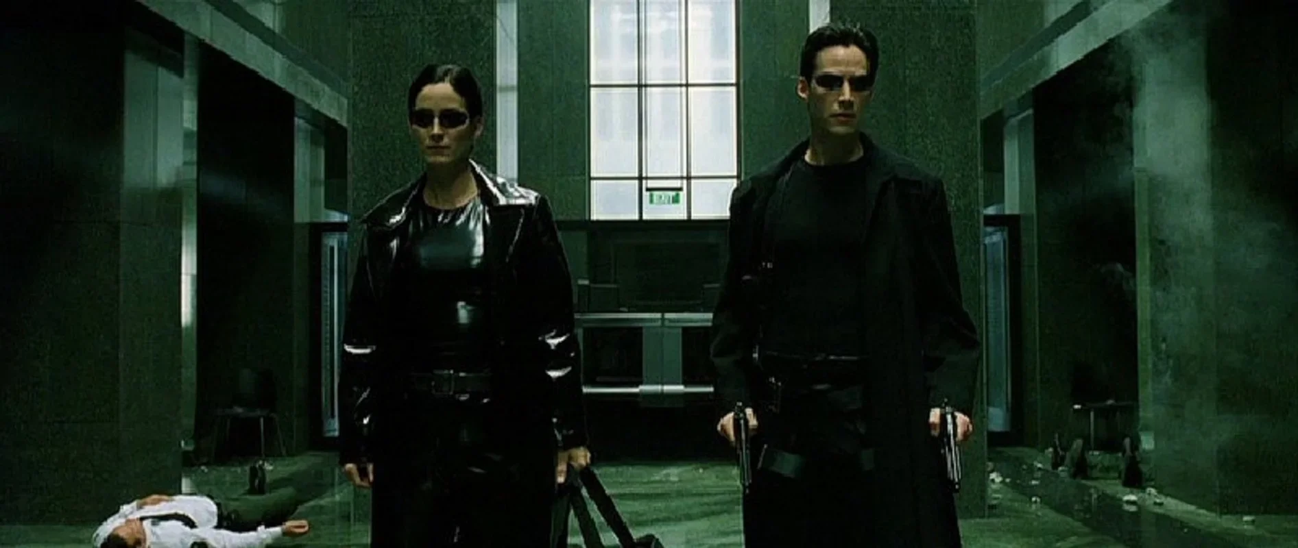 Scene from The Matrix, showing Neo and Trinity in black outfits and sunglasses standing in a dark green hallway after a gunfight.