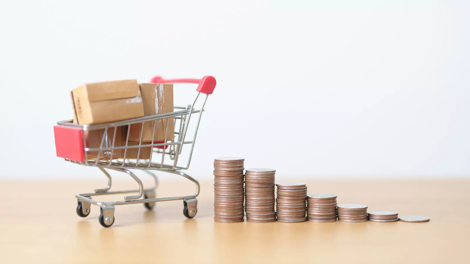 쇼핑카트에 담긴 택배 상자들과 그 옆에 점차 낮아지는 동전 탑 - 물가 상승 및 비용 절감을 통한 기업 재무 관리 필요성 강조