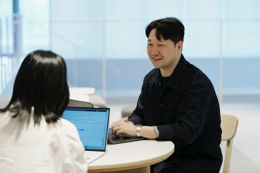 앳홈 팀원이 밝은 라운지에서 노트북을 앞에 두고 웃으며 대화하는 모습