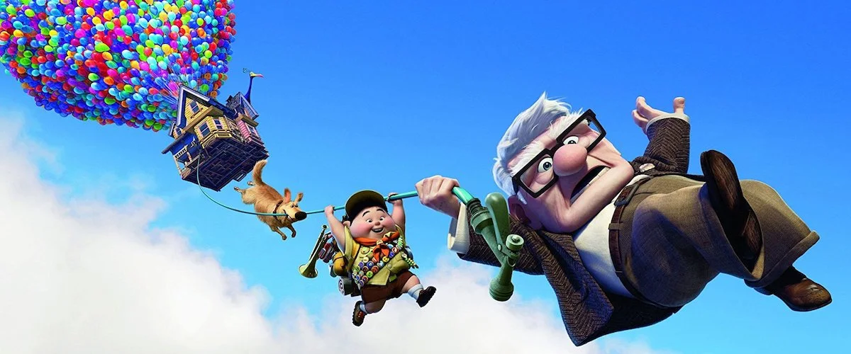 Scene from Pixar’s Up showing Carl Fredricksen, Russell, Dug, and a balloon-lifted house floating through the sky. The whimsical image illustrates how an impossible fantasy premise feels emotionally believable because Carl’s grief, fear, and attachment are grounded in deeply human emotion.