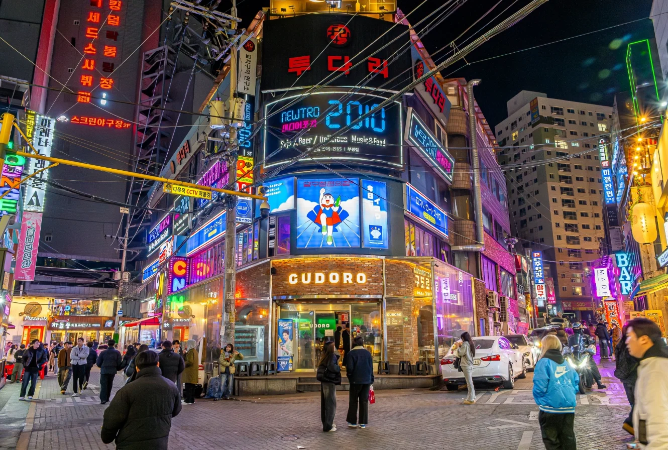 해질녘 상업 거리에서 LED 채널간판과 대형 LED전광판이 나란히 설치된 매장 외관, 보행자들이 전광판 콘텐츠를 바라보고 있다