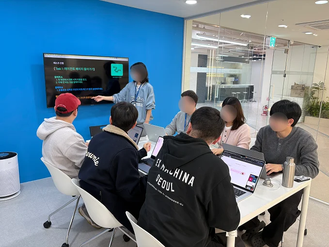 여러 명의 사람들이 모니터를 보며 수행해야 할 태스크를 확인하고 있는 모습