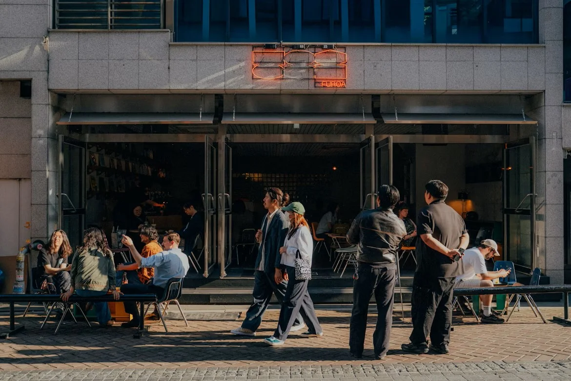 People sitting and walking outside a modern café in Seoul during a sunny afternoon.
