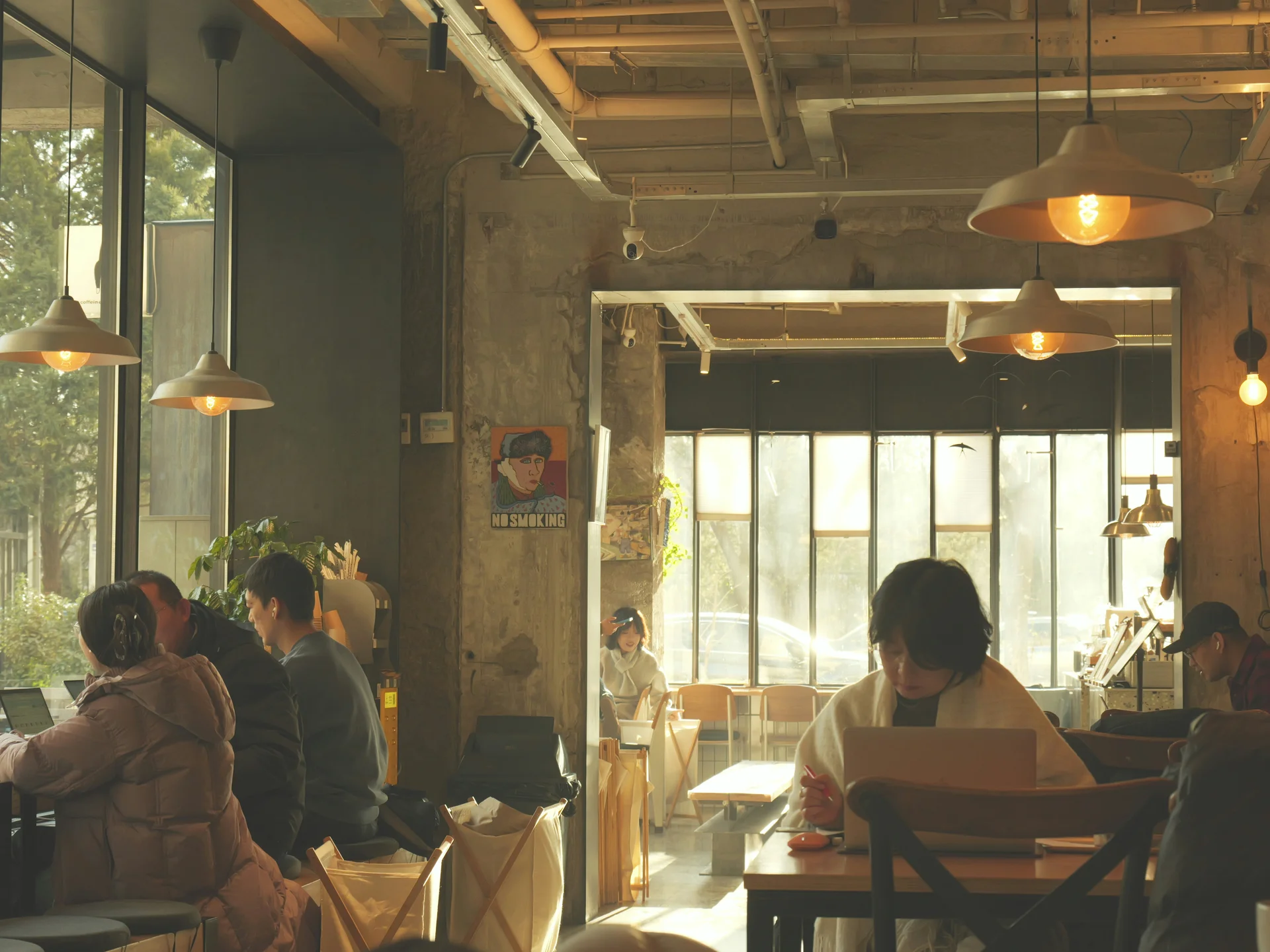 **Warm café interior with people quietly working and sunlight glowing through large windows.