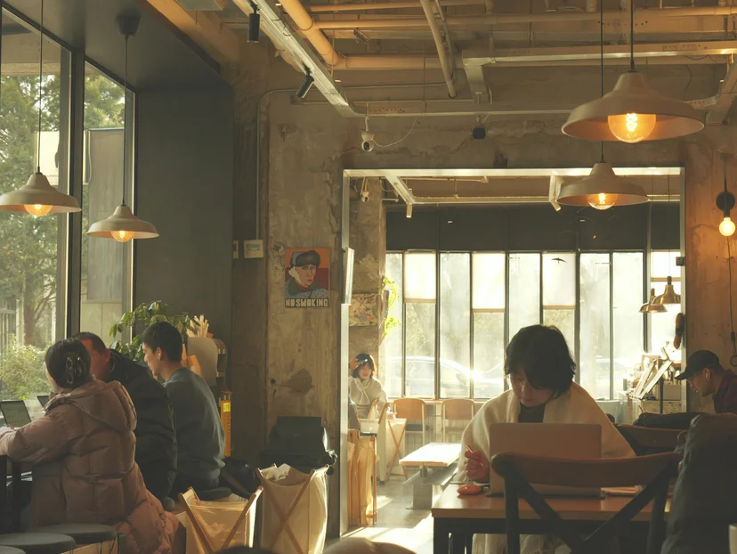 **Warm café interior with people quietly working and sunlight glowing through large windows.