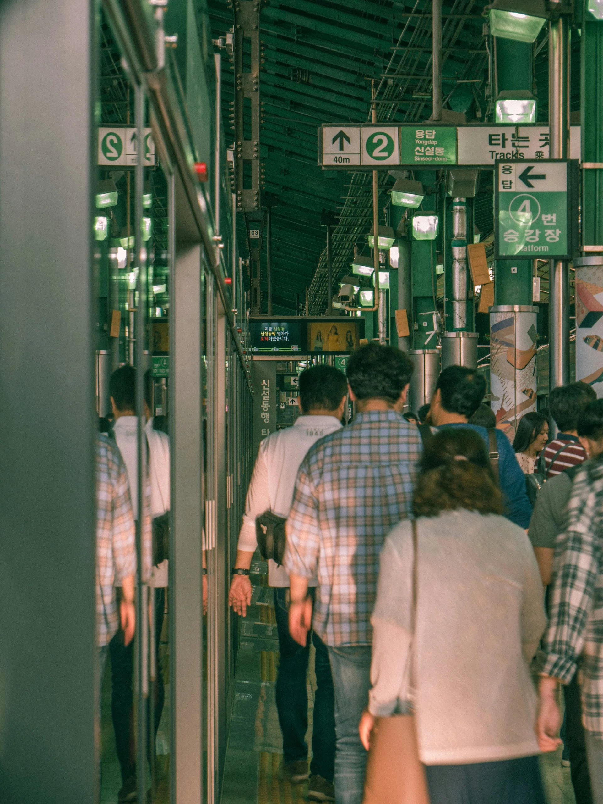 People walking along a busy subway platform under green station lights.