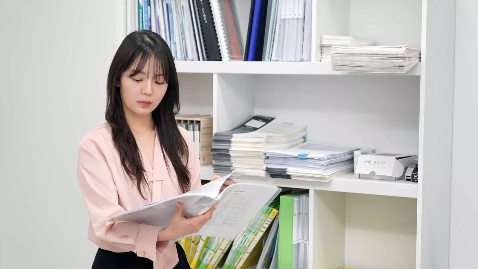 사무실 책장 앞에서 종이 서류를 검토하고 있는 직원