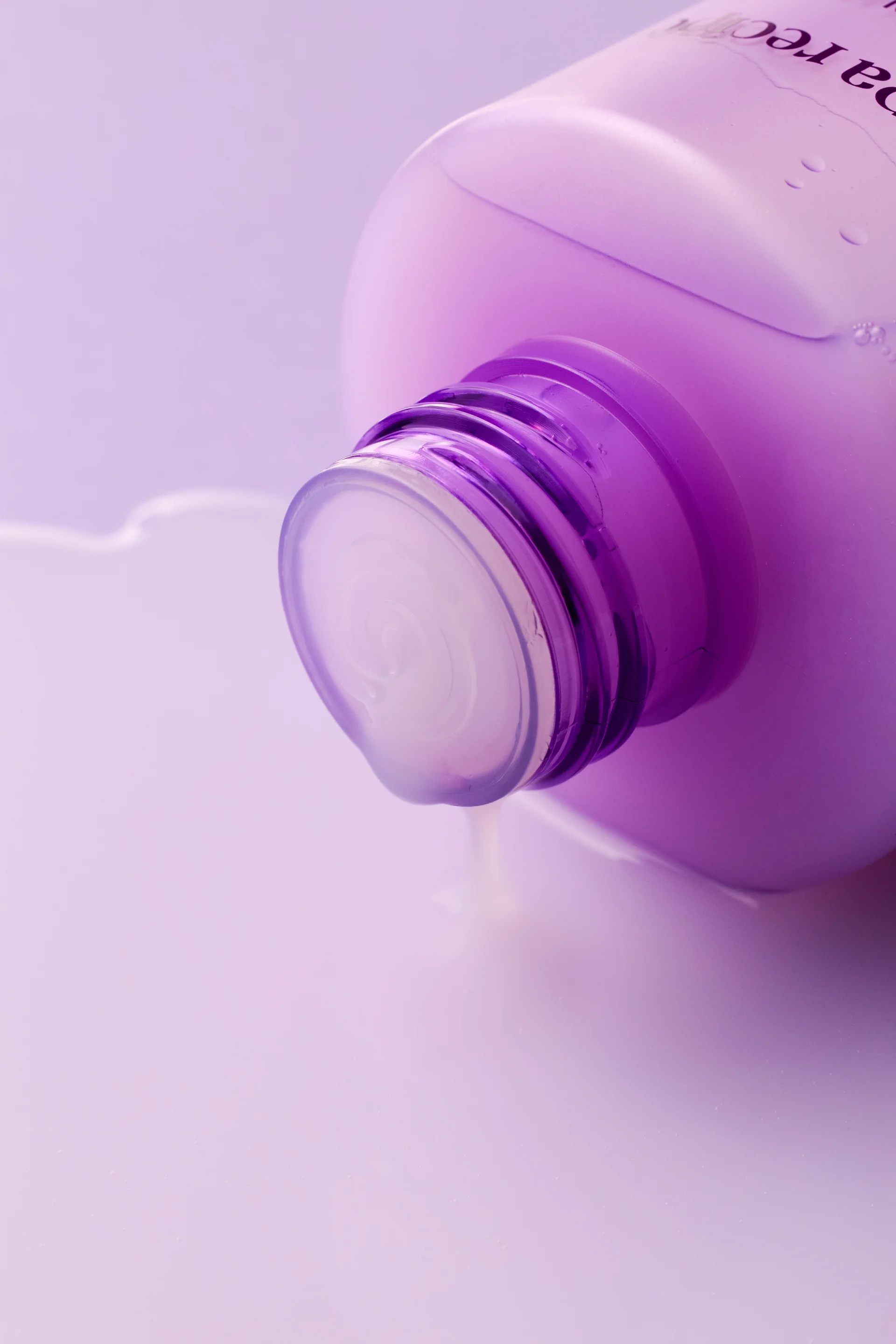 Papa Recipe Eggplant Clearing Pore Refine Toner bottle tipped on its side with cap open, pouring milky white toner liquid onto a lavender background