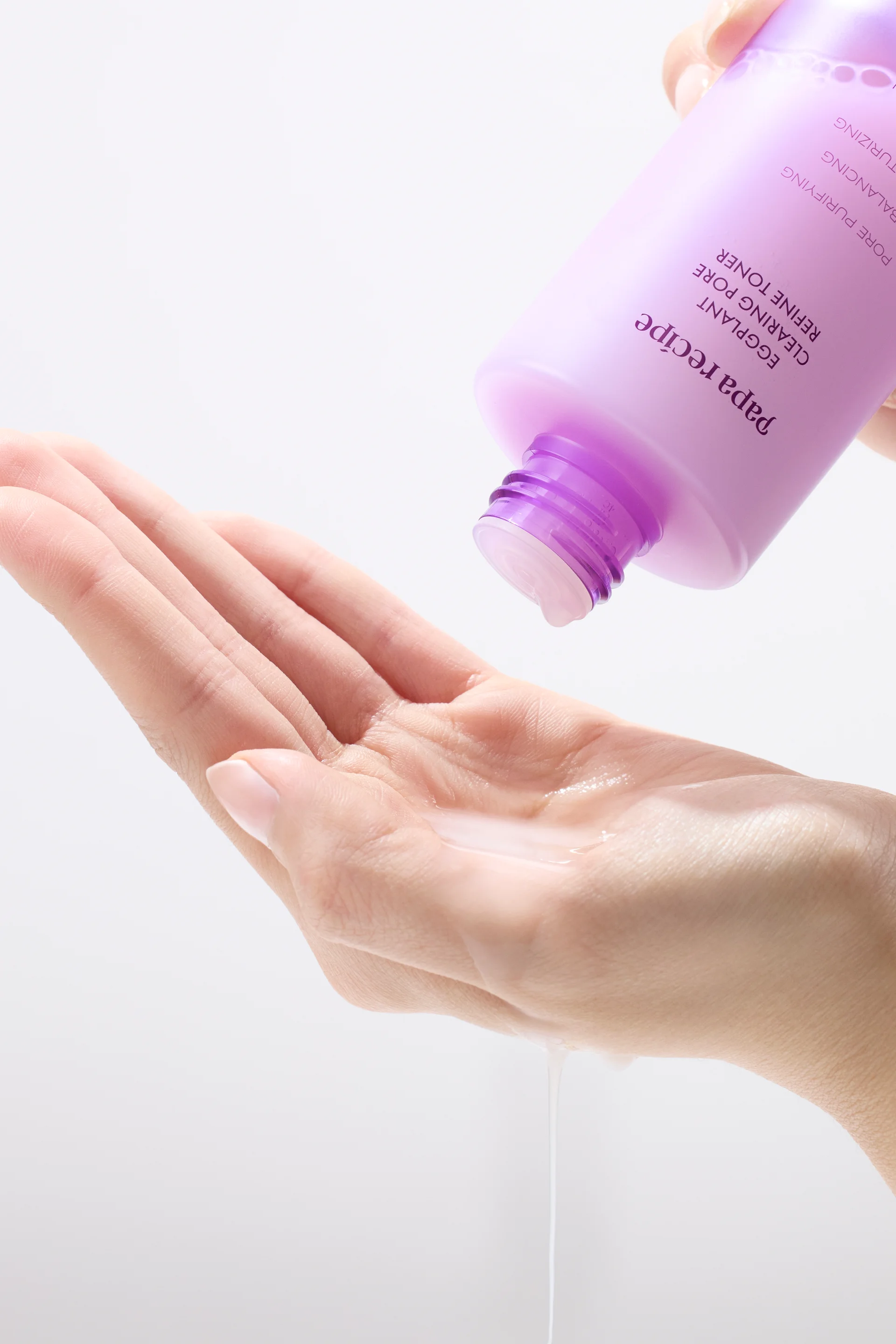 Papa Recipe Eggplant Clearing Pore Refine Toner bottle held upside down, dispensing milky toner onto an open palm against a white background