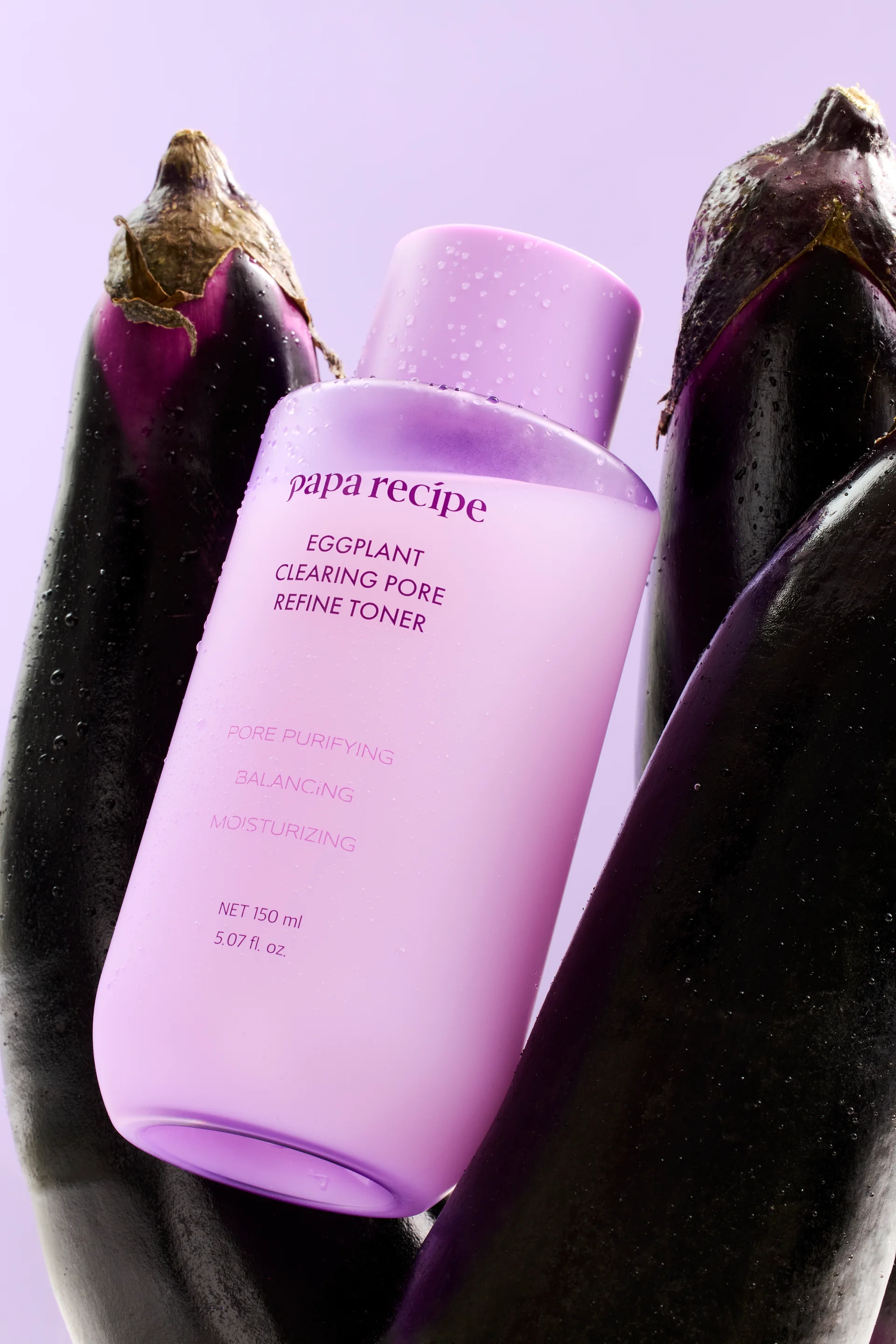Papa Recipe Eggplant Clearing Pore Refine Toner 150ml bottle with water droplets, nestled between two whole fresh eggplants against a lavender background