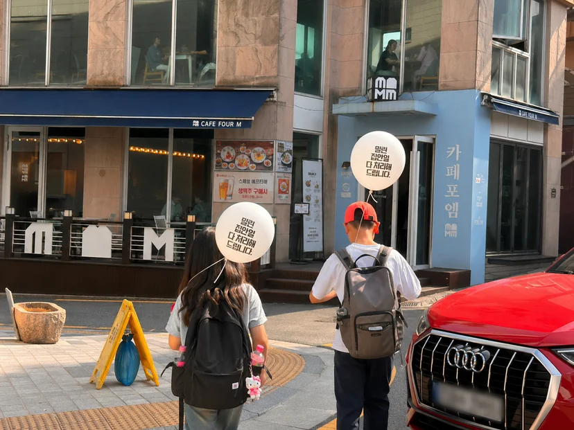 두 어린이가 밀린 집안일 다 처리해 드립니다 라고 쓰인 풍선을 들고 걸어가고 있다