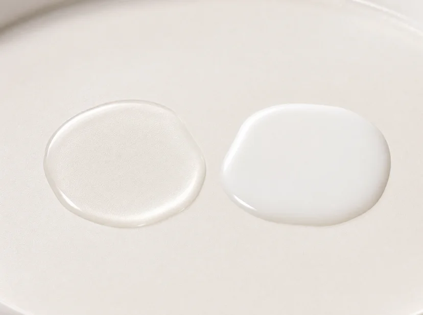 Close-up of two toner swatches side by side on a white ceramic surface — a thin, nearly transparent watery swatch on the left and a thicker, opaque milky white swatch on the right, showing the texture difference between an astringent toner and a milky toner