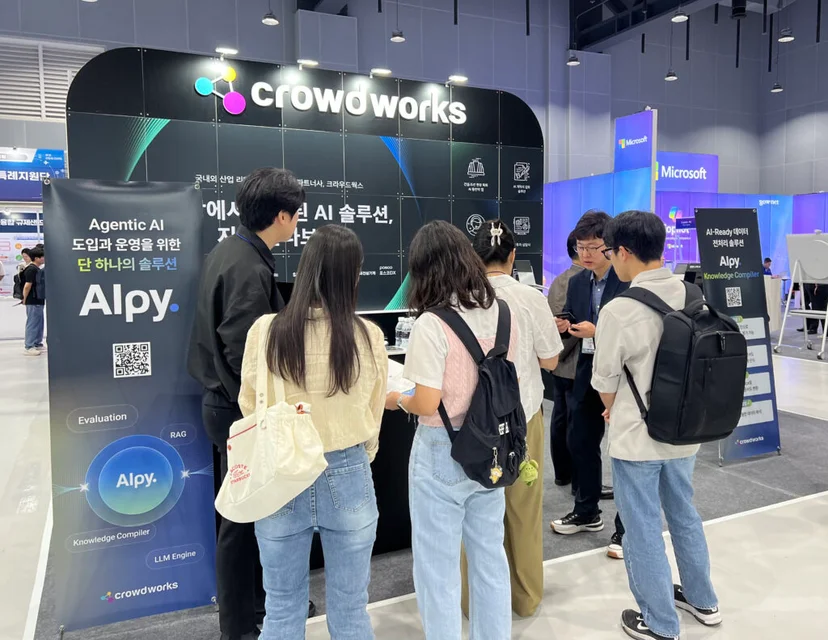 산업 AI EXPO 현장에서 크라우드웍스 부스를 방문한 관람객들이 AI 솔루션 ‘Alpy’에 대한 설명과 데모를 듣고 있는 모습. 배너에는 ‘Agentic AI 도입과 운영을 위한 단 하나의 솔루션 Alpy’라는 문구가 보임