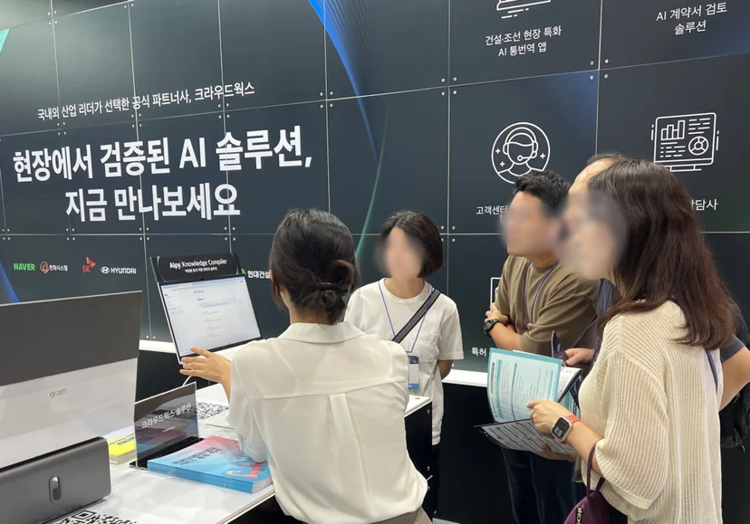 산업 AI EXPO 2025 현장에서 크라우드웍스 부스를 방문한 관람객들이 Alpy Knowledge Compiler 데모를 살펴보며 설명을 듣고있는 모습 