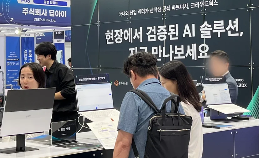 산업 AI EXPO 2025 현장에서 크라우드웍스 부스를 방문한 관람객들이 건설·조선 현장 특화 AI 통번역 앱 데모를 체험하며 설명을 듣고 있는 모습 