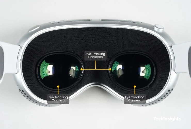  오후 6:18 Apple Vision Pro 내부 정면 사진. 양쪽 렌즈 안쪽에 내장된 아이트래킹 카메라 3개가 노란색 라벨로 표시됨. 실버 프레임과 검정 패브릭 소재의 페이스 쿠션이 보임.