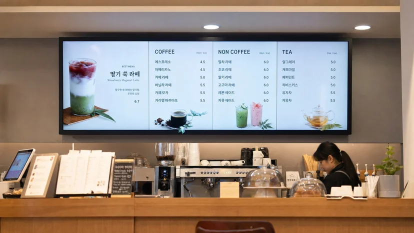 카페 카운터 위 디지털 메뉴보드가 메뉴와 가격을 표시하는 모습