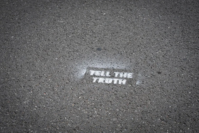 아스팔트 바닥에 스텐실로 찍힌 "TELL THE TRUTH" 문구, 진위를 확인할 수 없는 지원자의 진술을 상징하는 이미지