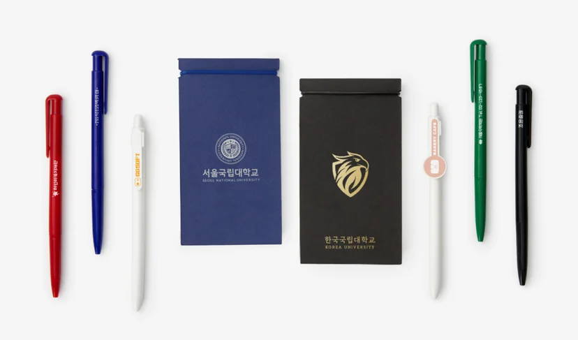 마플 대학 메모 수첩 – 서울국립대학교와 한국국립대학교 로고를 인쇄한 파란색·검은색 세로형 수첩과 다양한 색상의 볼펜을 흰 배경에 나란히 배치한 이미지
