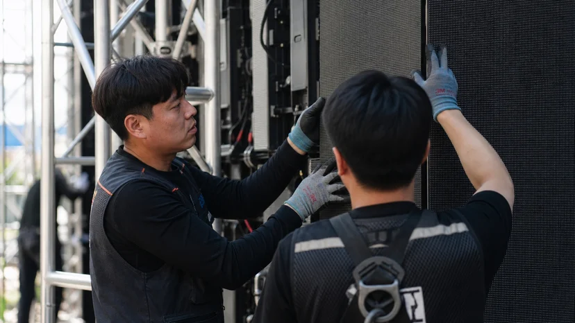 트러스 구조물에 LED 월 패널을 정렬해 조립하는 스튜디오 시공 현장의 작업자
