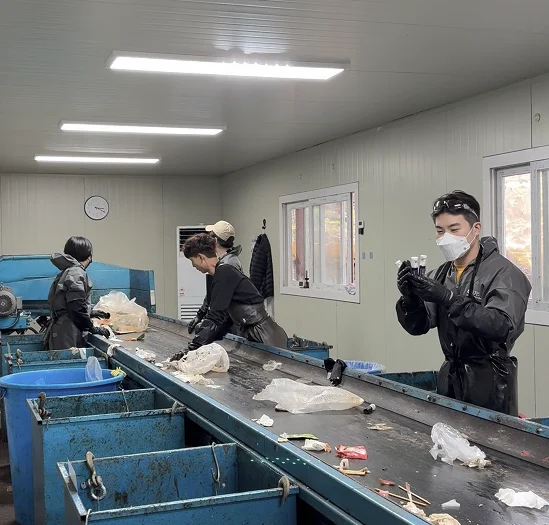 선별장 컨베이어 벨트 라인에 서서 재활용 품목을 선별 수거 분류하는 작업자들