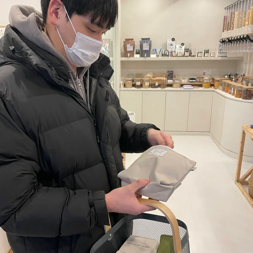 제로웨이스트 친환경 매장에서 마스크를 쓰고 쇼핑 바구니와 파우치 제품을 둘러보는 모습