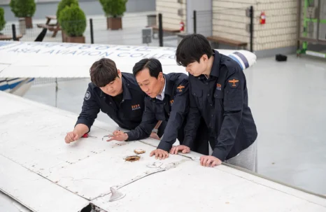 야외 항공기 날개 위에 세 사람이 손을 짚고 표면을 살피고 있는 모습