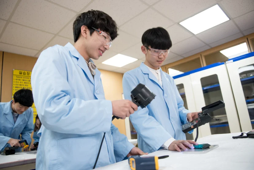 실습복 차림 두 사람이 작업대에서 케이블이 연결된 탐촉자와 장비를 사용하고 있는 모습