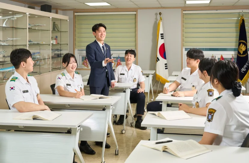흰 제복 차림 학생들이 책상에 앉아 교사의 설명을 듣는 모습