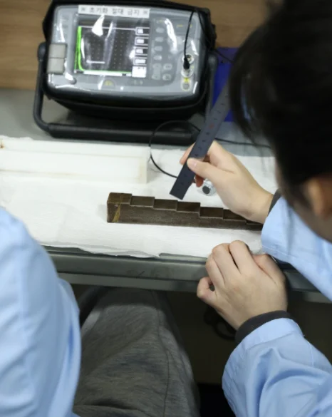 장비 화면 앞에서 사람이 금속 부품 위에 탐촉자를 대고 있는 모습