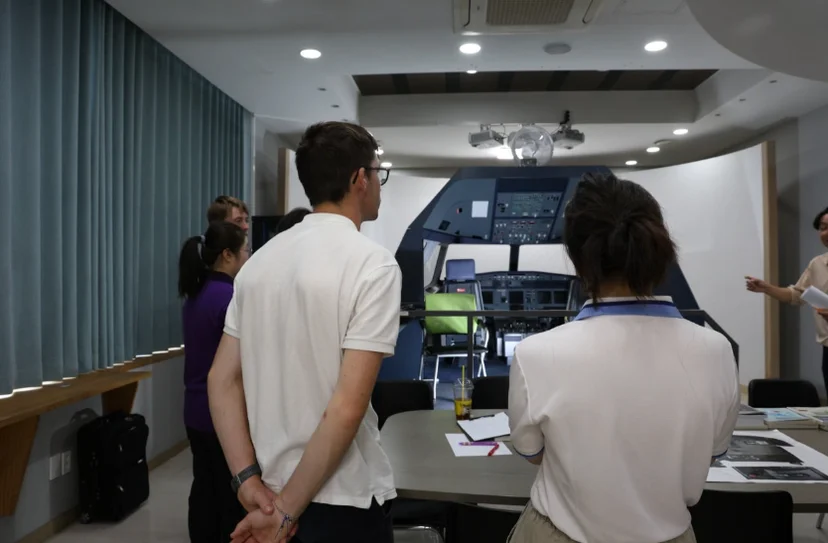 세 사람이 앞쪽 큰 화면에 표시된 조종석 장면을 바라보고 있는 모습