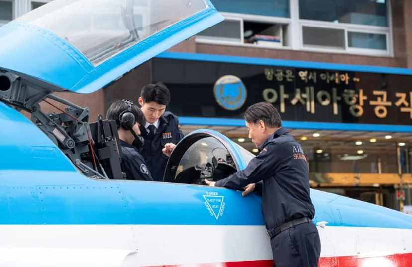푸른 항공기의 열린 조종석 주변에서 두 사람이 손으로 내부를 살피고 있는 모습