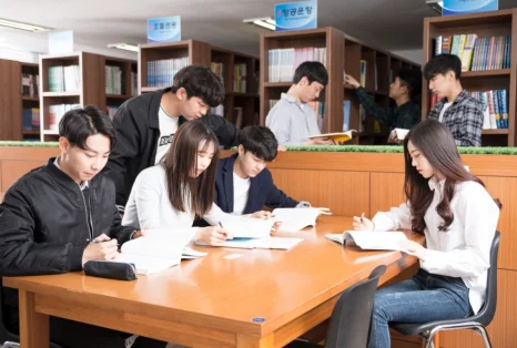 책장 앞의 큰 책상에 여러 사람이 둘러앉아 책과 종이를 보고 있는 모습