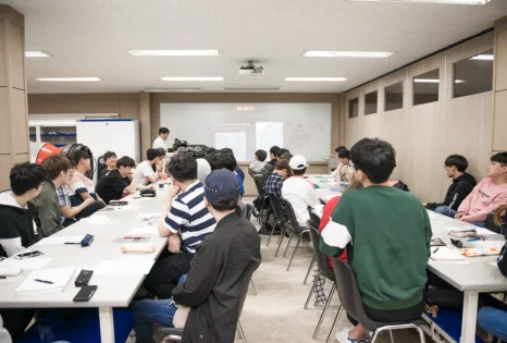여러 사람이 교실의 큰 책상에 모여 화면과 자료를 보고 있는 모습