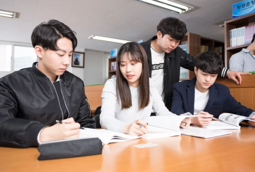 책장 앞의 책상에 여러 사람이 앉아 책을 읽거나 쓰고 있는 모습